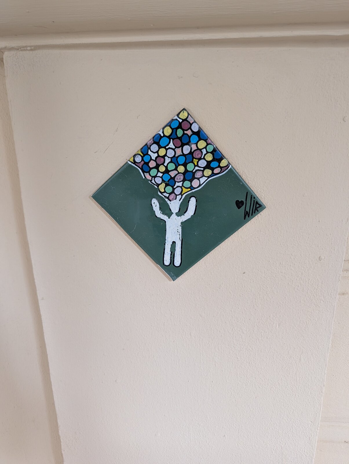 Fliese mit einer Figur, aus deren Kopf zahlreiche bunte Kugeln sprießen.