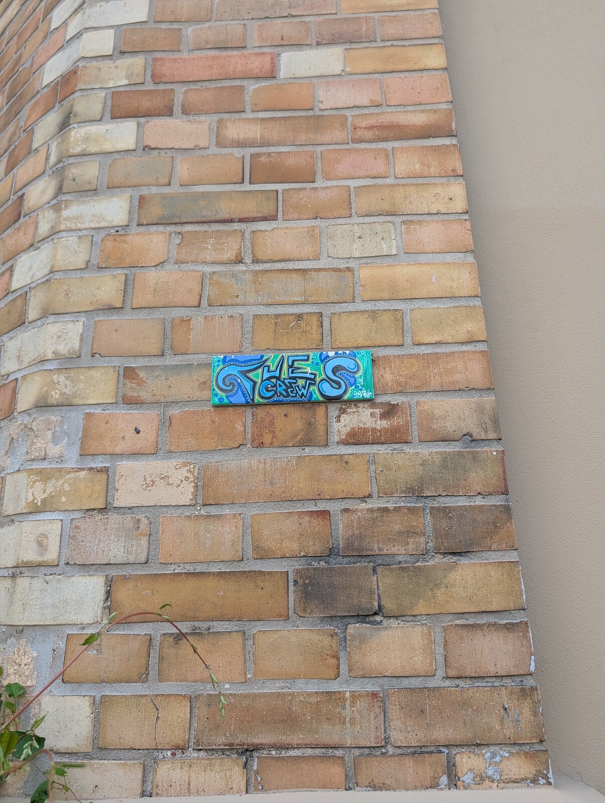 Ein farbiger Sticker auf Backsteinen einer Hauswand, der in Blau, Grün und Orange gehaltenem Tag mit verschlungenen Lettern zeigt.