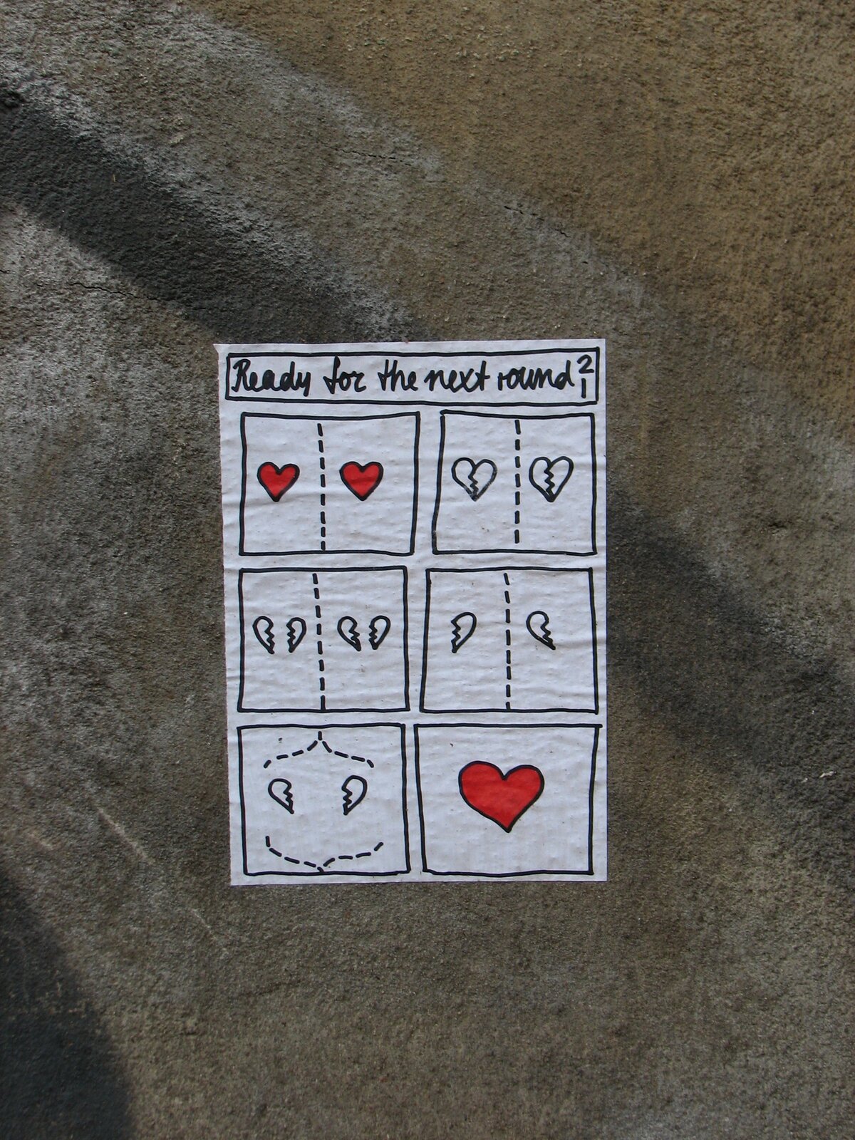 Auf grauem Untergrund angebrachter bemalter Papiersticker mit schwarzer Umrandung. Oben die Aufschrift 'Ready for the next round?', darunter ein 3x2-Raster aus sechs Feldern mit Herzmotiven in rot und schwarz, teils durchgestrichen, sowie Fragezeichen und