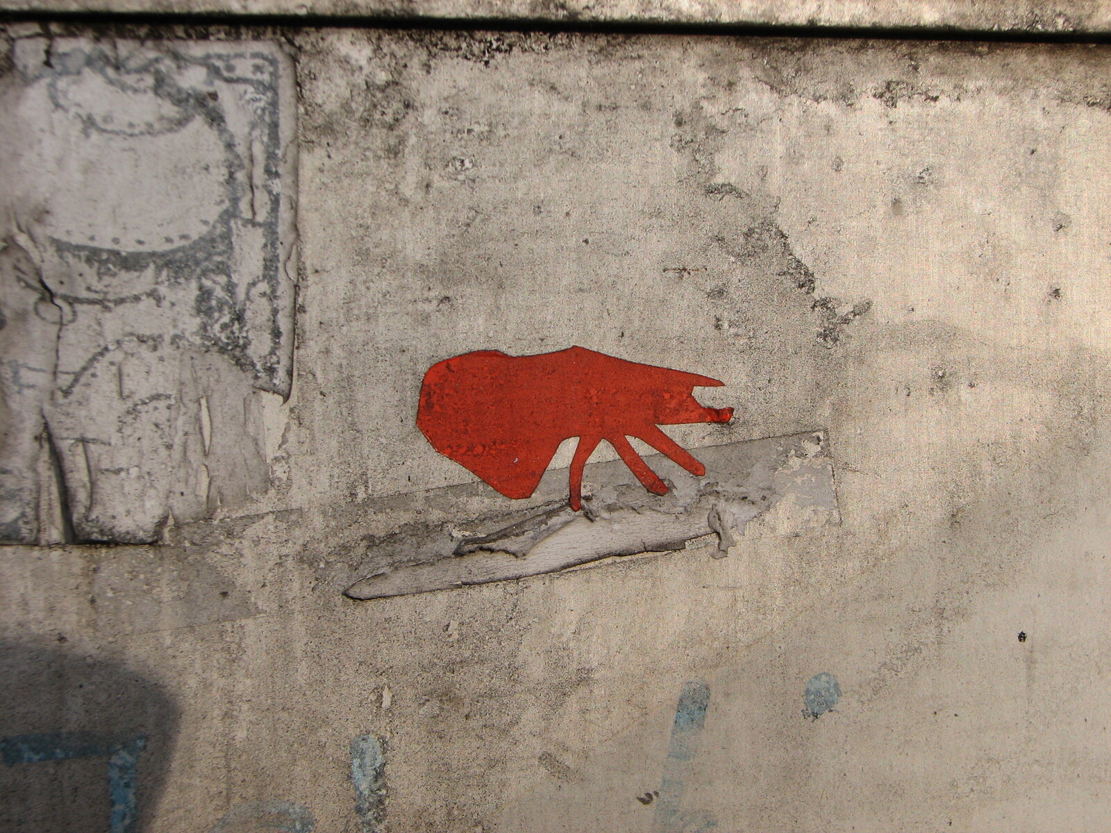 Rote Silhouette eines Insekts, möglicherweise eine Laus oder ein Floh, auf hellgrauer, verwitterter Betonwand. Die Figur ist schablonenhaft ausgeführt.